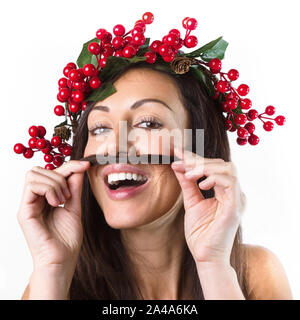 Carino santa donna con una ghirlanda di Natale sulla sua testa fa un grimace, baffi di capelli e guarda la fotocamera su sfondo bianco. Viso espressivo expr Foto Stock