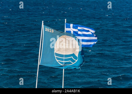 Elounda, Creta, Grecia. Ottobre 2019. La Bandiera Blu per una spiaggia eccellente battenti lungo con la bandiera nazionale della Grecia in Elounda, Creta. Foto Stock