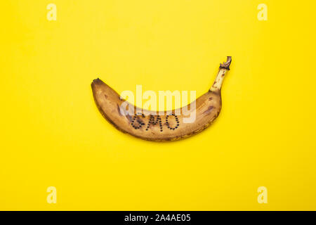 Surmature, annerite banana su cui la pelle la parola "OGM" è scritto giace su un brillante sfondo giallo. Foto Stock