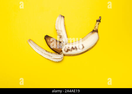 Surmature, annerite banana con un parzialmente pelato la pelle e la parola "OGM" scritto sulla pasta è su un brillante sfondo giallo. Foto Stock