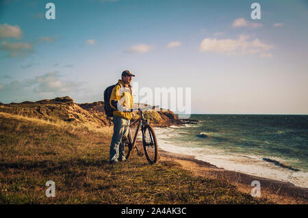 Escursioni in bicicletta in Irlanda. Ciclista ricreative con mountain bike e zainetto sul bordo delle dune di sabbia guardando il mare. Foto Stock