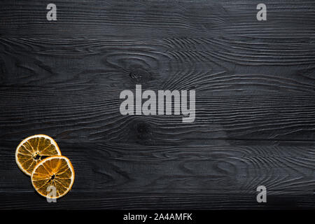 Arance essiccate le fette su legno nero, sfondo, vista dall'alto. Spazio per il testo. Natale gustoso concetto. Foto Stock