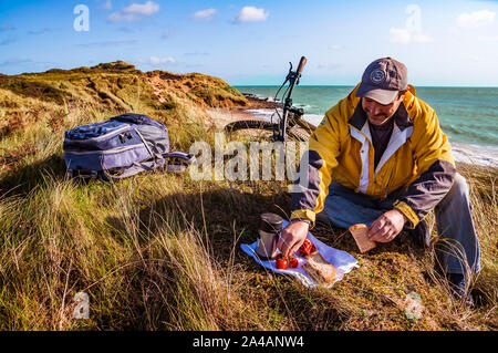 Mangiare fuori. La colazione sulle dune di sabbia in riva al mare. Ciclista ricreative avente la sua pausa pranzo. Foto Stock