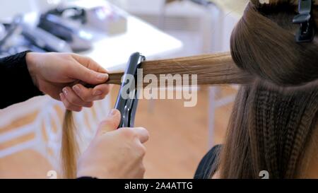 Parrucchiere con piastra sui capelli lunghi di client in parrucchiere Foto Stock