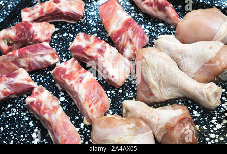 Pezzi di carne cruda e le cosce di pollo su una teglia da forno prima della cottura Foto Stock