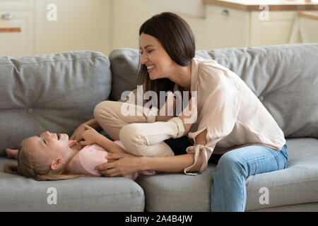 Ridendo madre solletico poco adorabile figlia, giocando sul lettino Foto Stock