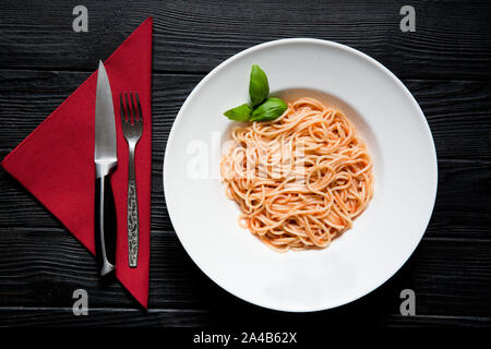 Vegetariano spaghetti con pomodoro, basilico e formaggio parmesane nero su sfondo di legno, servita con forcella e igienico sul velluto rosso igienico, vista dall'alto. M Foto Stock