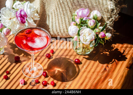 Rustico solenne ancora in vita con un bicchiere di rosso a bere con autunno bacche e ghiaccio circondati da fiori bianchi su sfondo tessili. Tavolo in legno nella st Foto Stock