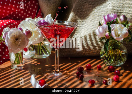 Natura morta con un bicchiere di rosso a bere con i frutti di bosco con un tocco e schizza di caduta di Berry. Circondato da fiori su sfondo tessili in striped s Foto Stock