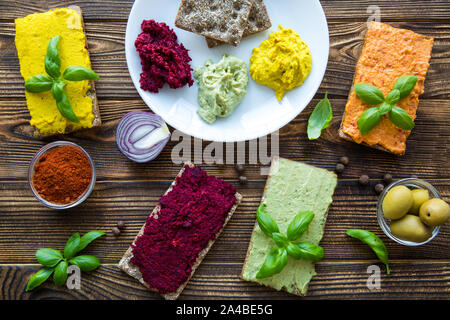 Diversi tipi di hummus sulla piastra bianca e pane sano marrone sul tavolo di legno. Colori luminosi di cibo. Foto Stock