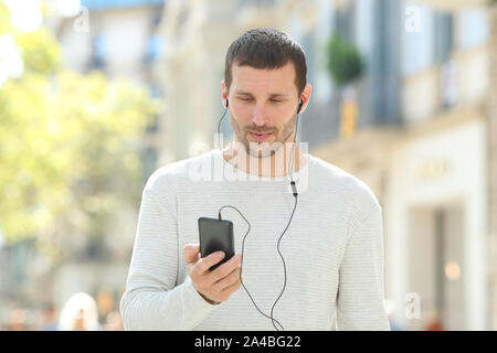 Vista anteriore verticale di un grave adulto uomo ascoltare musica sul telefono che indossa gli auricolari in strada Foto Stock