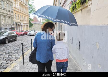Autunno piovoso meteo in città, Donna con bambina ragazza camminare sotto un ombrello in street, vista posteriore Foto Stock