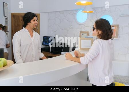 Resort hotel reception, donna valutazione parlando di uomo che lavora alla reception. Foto Stock
