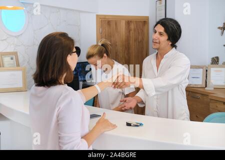 Controllo degli ospiti in hotel, maschio e femmina receptionist in piedi presso la reception a parlare e saluto donna valutazione Foto Stock