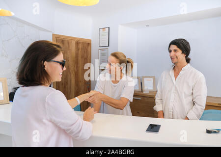 Controllo degli ospiti in hotel, maschio e femmina receptionist in piedi presso la reception a parlare e saluto donna valutazione Foto Stock