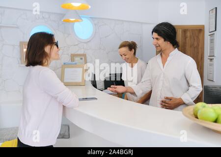 Ricezione presso il resort hotel. L uomo e la donna gli addetti della reception sul posto di lavoro. Valutazione il check in presso la reception Foto Stock