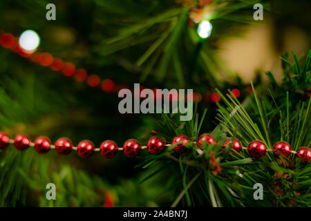 Catena di rosso le palle di Natale collocato su di un albero di Natale con sfondo sfocato in verde e giallo le tonalità e le luci e razzi. Foto Stock