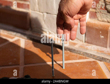 Una mano d'uomo riccioli di un dado su un asta filettata in una giornata di sole e con gli altri strumenti in un lavoro FAI DA TE Foto Stock