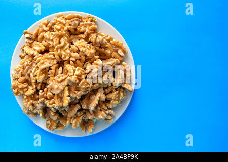 Pila di noci sulla piastra bianca isolata su sfondo blu. Snack sani e cibo. Vista dall'alto. Le noci Foto Stock