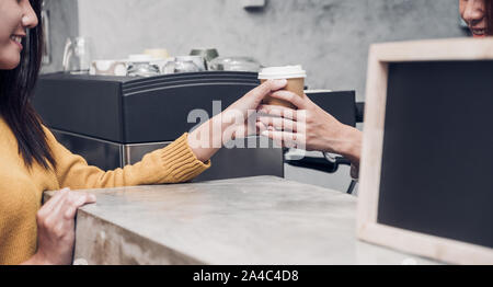 Giovane donna asiatica barista indossare jean grembiule serviva per andare tazza di caffè al cliente al banco bar con sorriso emozione,Cafe Restaurant service concetto,proprietario Foto Stock