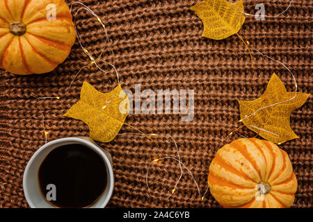Autunno cornice fatta di zucche, una tazza di caffè e foglie cadute sul marrone felpa lavorata a maglia. Caduta, Halloween e concetto di ringraziamento. Vista dall'alto. Vuoto Foto Stock