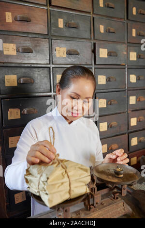 Positivo tradizionali asiatici speziale lavoratore mettendo cadono su scale e pacchetti di ponderazione con trattamento per il cliente Foto Stock