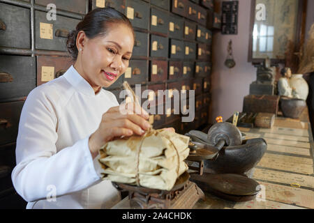 Senior donna che lavorano in cinese tradizionale farmacia e pacchetti di ponderazione Foto Stock