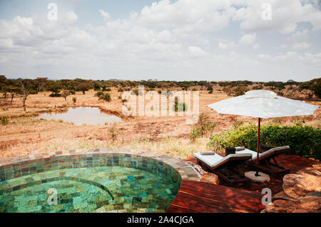 JUN 20, 2011 Tanzania - piscina di lusso africano safari lodge terrazza con ombrellone bianco e la piscina letto nella foresta di savana del Serengeti Grumeti selvatica Foto Stock