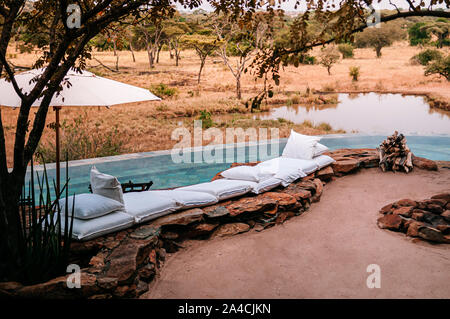 JUN 20, 2011 Tanzania - Piscina e lusso africano safari lodge terrazza con cusions bianco e ombrellone nella foresta di savana del Serengeti Grumeti w Foto Stock