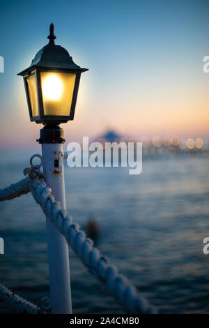 Una lanterna su un molo si illumina di colore giallo brillante al crepuscolo Foto Stock