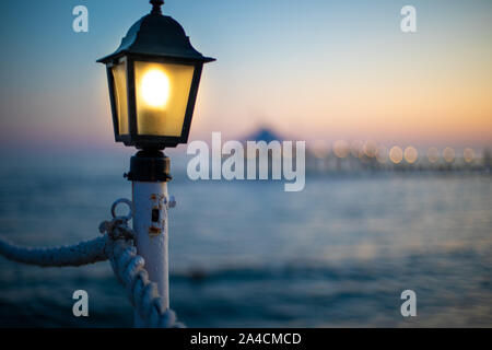 Una lanterna su un molo si illumina di colore giallo brillante al crepuscolo Foto Stock