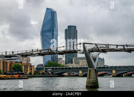 La gente cammina sul Millennium Bridge che attraversa il Tamigi, a Londra. Uno Blackfriars Tower (alias The Vase) e South Bank Tower sono sullo sfondo Foto Stock