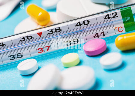 Termometro con una temperatura di 40 gradi con varie pastiglie su uno sfondo blu. Il concetto di scelta di una medicina fredda Foto Stock