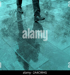 Sfocate gambe di riflessione e di ombra, silhouette di un uomo in un marciapiede in umido in una pozza camminando su un sensore pioggia