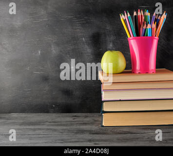 Pila di libri e multi-colore matite in legno, sullo sfondo di un vuoto di gesso nero bordo, torna al concetto di scuola Foto Stock