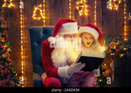 Babbo Natale dando un presente per un po' stupito carina ragazza in pigiama e santa hat Foto Stock