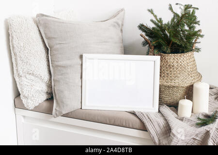 Vuoto bianco telaio in legno mockup con albero di Natale, candele, biancheria cuscini e plaid sul banco di bianco. Poster design di prodotto. Scandinavian home Foto Stock