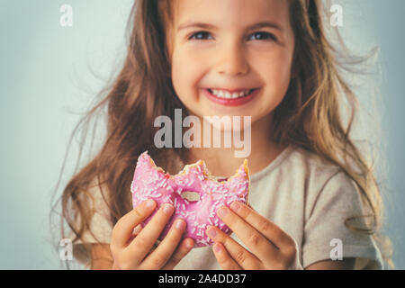 Sweet little girl mangiare ciambella rosa. Foto Stock