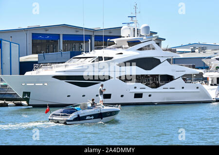 Le persone sulla piccola imbarcazione a motore passando ormeggiati lussuosi yacht a motore prodotto dalla Sunseeker il successo aziendale presso il proprio cantiere & fabbrica presso il porto di Poole Dorset UK Foto Stock