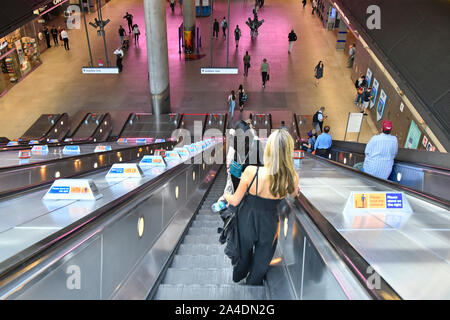 Giovane donna & altri passeggeri scendono sulla scala mobile al tubo della metropolitana treno servizi a Canary Wharf stazione ferroviaria Docklands di Londra Inghilterra REGNO UNITO Foto Stock