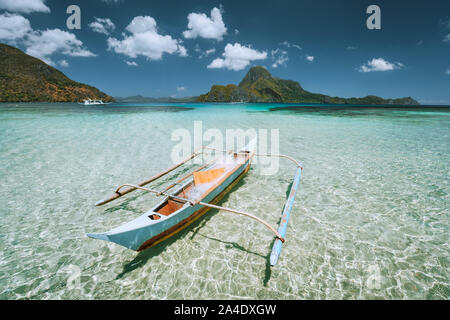 Palawan, Filippine. Tradizionale piccola pesca barca banca di fronte Cadlao Island in cristalline acque poco profonde durante la bassa marea. Foto Stock