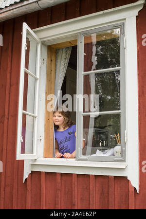 Giovane ragazza in una finestra aperta su un cottage di campagna, Svezia. Foto Stock