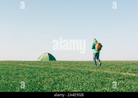Turistico con zaino andando a la sua tenda sul campo estivo. Concetto di viaggio Foto Stock
