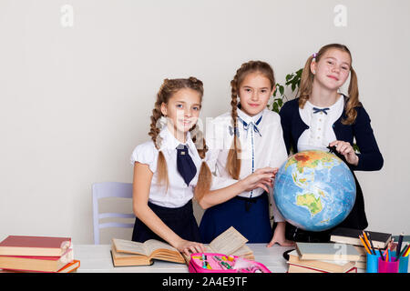 Tre studentesse presso il desk studio il globo in una geografia di classe Foto Stock