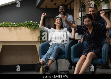 Quattro diverse etnicità impiegati divertirsi a cavallo su sedie Foto Stock
