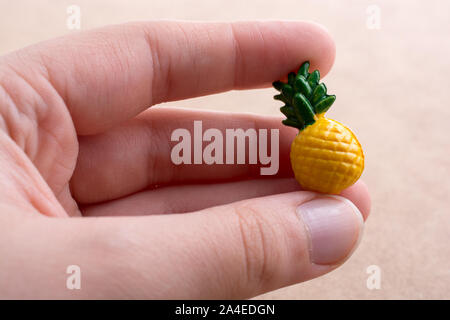 Mano che tiene un piccolo ananas miniatura su uno sfondo sul display Foto Stock