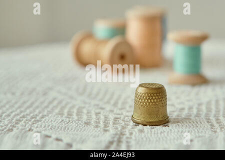 Ottone Vintage ditale di close-up. È su una vecchia maglia fatti a mano tovaglia. Sullo sfondo di legno vintage bobine con fili di cucitura. Foto Stock