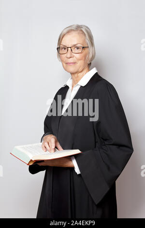 Avvocato femmina concetto: ritratto di una donna anziana in un abito nero tenendo un testo legislativo libro. Foto Stock