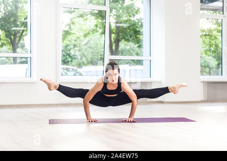 Full lenght Ritratto di giovane adulto gumnastics bella donna in pantaloni neri e la parte superiore fa parte stand split, praticare esercizi yoga. Indoor, st Foto Stock