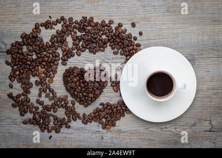 Caffè espresso su di un tavolo di legno con i chicchi di caffè in forma di cuore Foto Stock